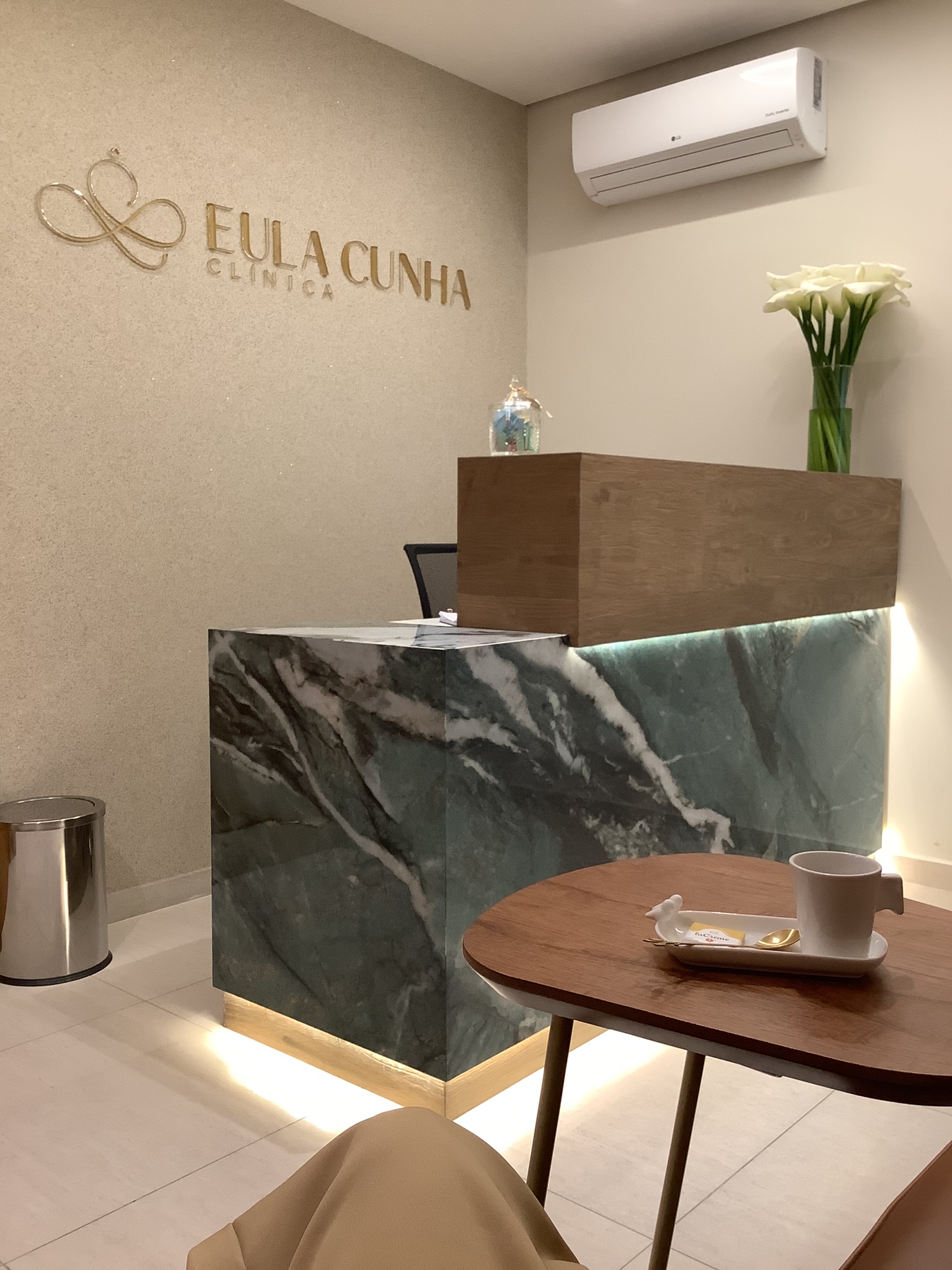 Recepção da Clínica Eula Cunha — logo dourada na parede e balcão de mármore verde