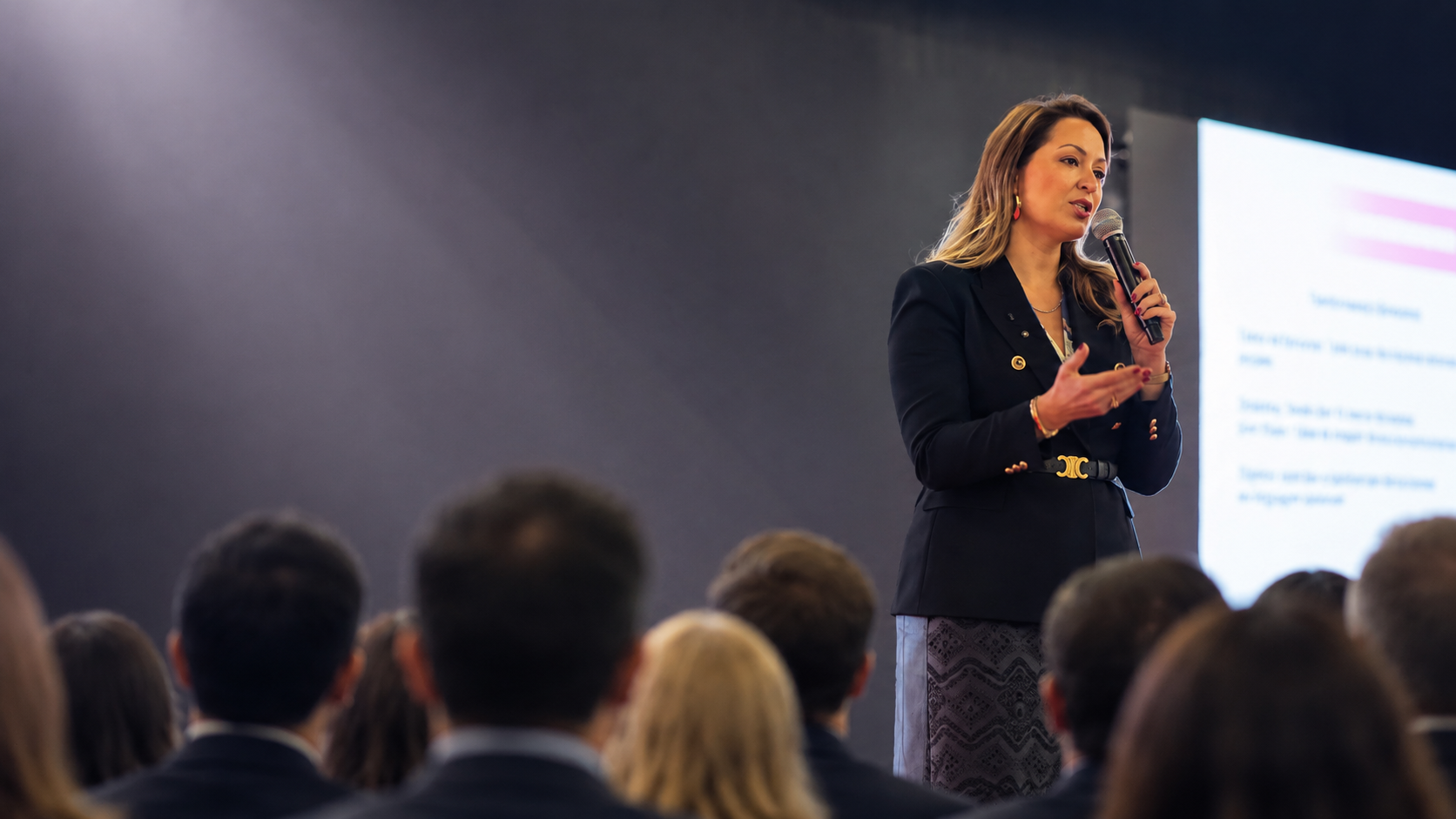 Eula Cunha ministrando palestra com microfone para plateia em evento corporativo